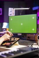 Professional artist using mixing console to edit tracks, watching online tutorials on monitor with greenscreen, post production. Songwriter producer edits songs, control panel amplifier. photo