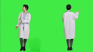 Physician pointing to the left or right to create web commercial standing against greenscreen backdrop, doing a marketing advertisement in studio. Woman medic in white coat shows an ad. Camera A. photo