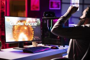 Upset gamer at desk frustrated after receiving game over screen, getting his spaceship destroyed in flying game. Sad player feeling gutted after losing science fiction videogame photo