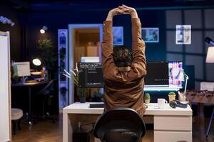 Developer doing software quality assurance, stretching after reading source code, feeling tired. IT admin relaxing muscles after inspecting coding to fix potential issues all day photo