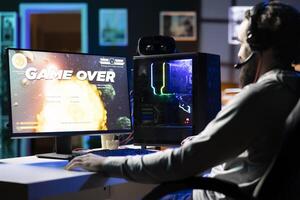 Man wearing headphones upset after losing while playing online spaceship videogame. Sad player disappointed after getting flying spacecraft destroyed in game, getting game over screen photo