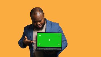 Portrait of african american man doing influencer marketing using green screen lapyop, studio background. BIPOC person holding empty copy space mockup notebook, doing advertising camera A photo