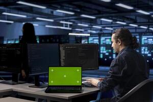 Engineer using green screen laptop to oversee servers used for managing databases, hosting websites and storing files. Employee working on mockup notebook in data center storing information photo