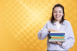 Portrait of joyful woman laughing while holding pile of books, enjoying reading hobby. Joyous person grinning, satisfied with stack of novels in arms, enjoying leisure time, studio background photo