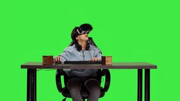 POV of woman player using vr headset to participate in online shooter contest at her computer, sitting at desk against greenscreen backdrop. Gamer playing games with virtual reality. Camera B. photo