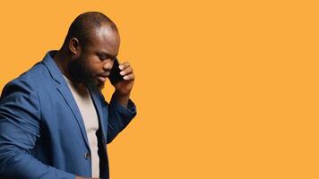 African american man enjoying talking with friends phone call using smartphone, studio background. BIPOC person walking around conversating during telephone call, camera A photo