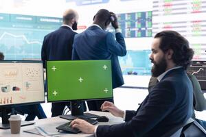 Business manager analyzes reports next to a green screen on pc, working with infographics and sales for development. Analyst consultant looks at isolated mockup display in office. photo