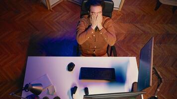 Top down view of software engineer putting face in hands in frustration while updating binary code script on computer, receiving errors. IT worker exasperated by annoying bugs while programming, aerial shot photo