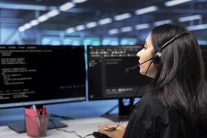 IT support personnel in data center talking in headphones microphone, doing checkup. Woman at work in server hub chatting with on field engineer, monitoring servers infrastructure photo