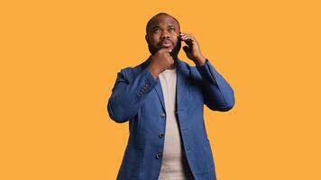 African american man having thoughtful conversation with friend during telephone call, studio background. Pensive BIPOC person talking on phone with mate, doing thinking gesturing, camera B photo