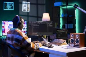 African american computer scientist in home office programming code on pc. Freelancing developer solving tasks for an IT job, writing lines of code at his personal office, cybersecurity. photo