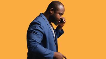 African american man enjoying talking with friends phone call using smartphone, studio background. BIPOC person walking around conversating during telephone call, camera B photo