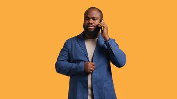 African american man disagreeing with friend during telephone call, shaking head, studio background. BIPOC person talking on phone with mate, unhappy with proposal, refusing, camera B photo