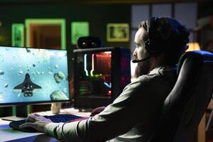 Man plays online multiplayer spaceship videogame with friends, using headphones for immersive experience. Player using gaming setup to flying spacecraft in flight game, enjoying leisure time photo