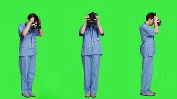 Medical assistant working with virtual reality glasses against greenscreen backdrop, using interactive 3d vision on vr headset to do checkup examination. Young nurse uses modern gadget. Camera A. photo