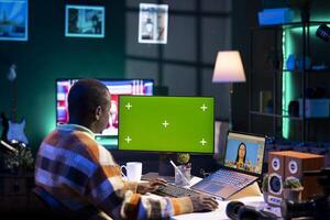 African american photo designer retouching images next to green screen on dual screens in a tech driven environment, representing modern digital media. Male graphic artist uses software tools.