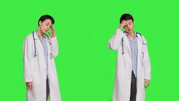 Unhappy medic dealing with a painful migraine against greenscreen backdrop, working in healthcare industry under pressure. Woman physician suffering from a headache, overworked. Camera B. photo