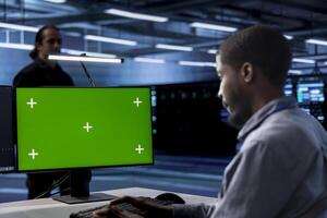 Employee using green screen PC to check for signs of imminent failure in data center supercomputers. Engineer working at chroma key PC to prevent damages in server farm, monitoring critical systems photo