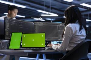 Coworkers in data center using green screen laptop and tablet to find firewall misconfigurations affecting servers. Colleagues in server room checking systems bottlenecks using mockup devices photo
