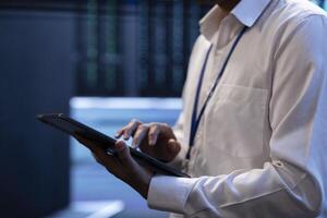 Engineer working in high tech server farm, using laptop and tablet to analyze data, ensuring seamless data flow. Man examining hardware in data center, ensuring system integrity and security, close up photo