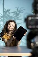 Happy entertaining woman in studio films tablet review for tech enthusiasts. Joyous online star hosts technology internet show, unboxing digital portable device, feeling impressed by thinness photo