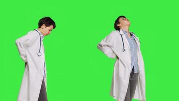 Woman physician experiencing lower back acute pain in studio, suffering from scoliosis and having muscles discomfort. Medic dealing with backache from burnout, greenscreen backdrop. Camera B. photo