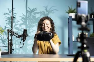 Happy tech specialist reviewing futuristic VR goggles in studio. Smiling entertaining media star filming technology channel vlog for gadget enthusiasts, showcasing virtual reality glasses photo