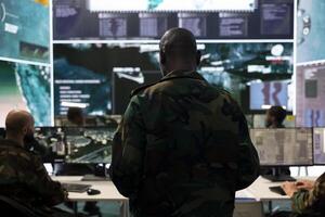 Infantry unit trooper collecting intelligence for a field operation, working with high tech reconnaissance gear and a big screen. Military staff analyzes real time data, surveillance support. photo