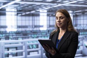 Technician in server hub checking recovery plan on tablet, monitoring energy consumption across supercomputers. Woman in data center making sure rigs are functioning optimally photo