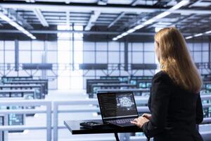 IT expert in data center updating AI systems, writing intricate binary code scripts on laptop. Certified admin using programming to upgrade artificial intelligence simulation model photo