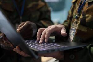 Diverse military staff analyzing battlefield data via satellite imagery on a laptop, transmitting crucial information for an infantry operation. Recruits team working in army power base. Close up. photo