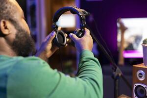Trained audio technician picking up his headset for a recording session, mixing and mastering his tracks on digital software and stereo console. Music producer editing sounds. Close up. photo