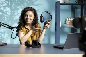Cheerful content creator reviewing newly released wireless headphones, comparing features with older models. Smiling audiophile filming for online channel, analyzing listening devices photo