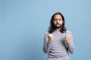 Male person feeling joyful and enthusiastic against blue background, being positive and cheerful about good news. Ecstatic pleased man feels satisfied and confident in front of camera. photo