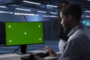 Admin in data center running system diagnostic tests using green screen computer display. Worker in server room deploying error checking utilities on chroma key desktop PC to repair network issues photo