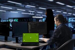 Admin in data center uses green screen laptop to update systems, protecting servers from software vulnerabilities. IT specialist uses mockup notebook to look for errors affecting servers photo