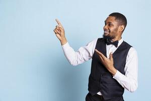 Hotel concierge pointing at something to the left or right on camera, indicating the direction for facilities at the five star lodging. Doorkeeper wearing a tuxedo at his job. photo