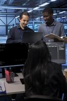 Cheerful teamworking engineers in data center looking for firewall misconfigurations affecting servers. Happy multiethnic employees checking systems bottlenecks leading to sluggish data transfer rates photo