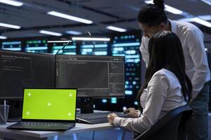 Isolated screen laptop in data center delivering immense computing power, capable of processing and storing data. Chroma key notebook in front of engineers fixing server racks rows photo