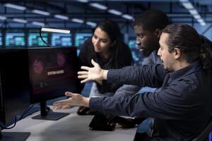 Team of programmers in server hub facility frightened by hacker passing firewall and stealing data. Multiracial colleagues panicking after seeing security breach notification on monitor in data center photo