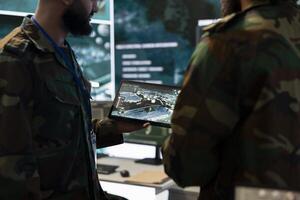 Army IT professional team examining satellite imagery on a tablet, gathering real time battlefield data for a national safety operation. Telecommunications staff work in control room. photo
