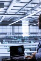 Software developer in data center using laptop to visualize artificial intelligence neural networks made up of interconnected nodes. Server room worker oversees AI systems processing information photo