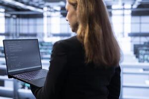 Engineer in data center tracking network traffic and activity, installing and configuring software updates using laptop. IT employee performing database backups to protect user information photo