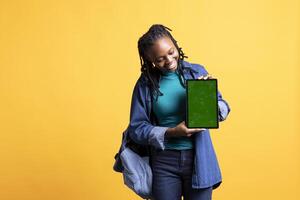 Upbeat african american woman presenting tablet with chroma key display, isolated over studio background. Happy BIPOC girl creating promotion with blank copy space mockup digital device photo