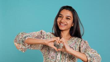 Portrait of smiling loving woman doing heart symbol shape gesture with hands, showing kindness. Happy affectionate girlfriend doing tender love gesturing for boyfriend, studio background, camera B photo