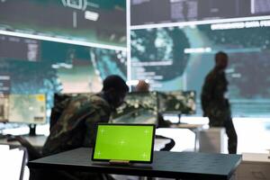 Military headquarters monitoring room with a mockup green screen on tablet, safeguarding the national territory from hostile warships. Skilled trooper serving the country in command center. photo