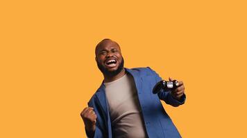 Joyous BIPOC gamer celebrating after winning gaming console game, studio background. Delighted man bragging after being victorious in videogame, defeating all enemies using gamepad, camera B photo