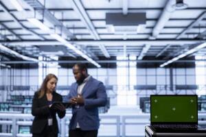 Focus on mockup laptop used by coworkers in data center ensuring cybersecurity and efficient network management. Close up of green screen notebook in server hub optimizing data center equipment photo
