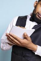 Hotel porter bellhop writes guests requests on smartphone call, discussing about amenities included in the room price. Doorkeeper staff takes notes with a list of guests in the ledger. photo