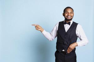 Hotel concierge pointing at something to the left or right on camera, indicating the direction for facilities at the five star lodging. Doorkeeper wearing a tuxedo at his job. photo